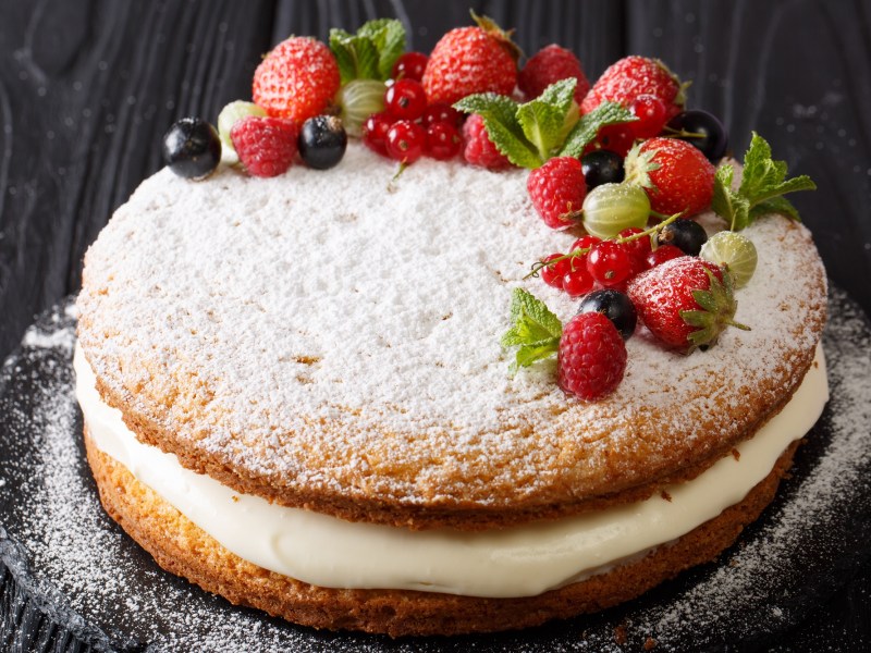 A Victoria Sponge Cake layered with cream, dusted with powdered sugar, and garnished with fresh berries.