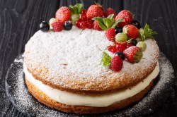 A Victoria Sponge Cake layered with cream, dusted with powdered sugar, and garnished with fresh berries.