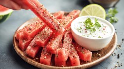 Watermelon fries with dip on a plate. Someone is taking a fry.