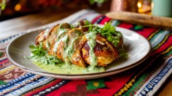 Plated pollo peruano drizzled in bright green sauce with chopped parsley.