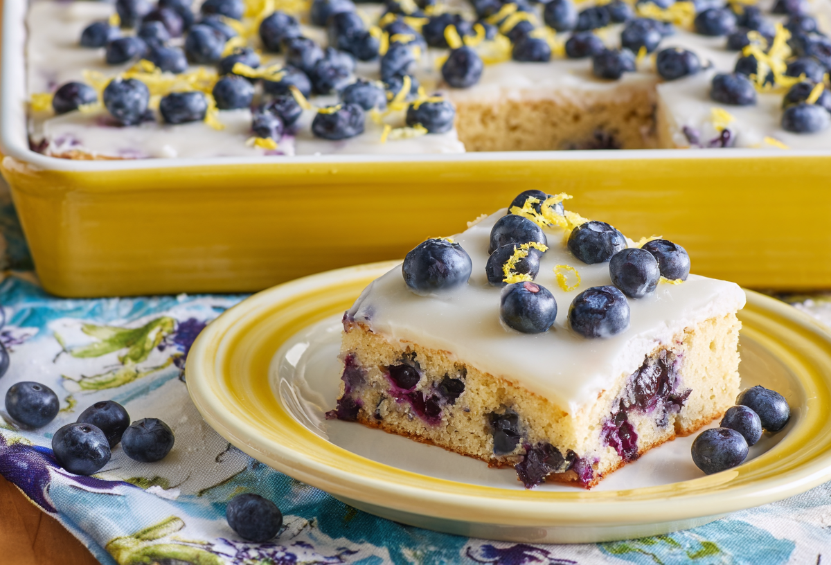 A piece of blueberry lemon sheet cake. The rest of the cake is in the background.