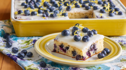 A piece of blueberry lemon sheet cake. The rest of the cake is in the background.