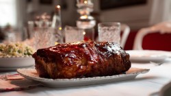 A Coca-Cola glazed pork loin on a plate in the dining room in full frontal view in white lighting.