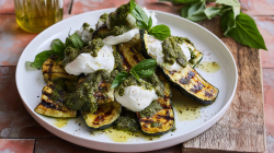 Grilled zucchini with burrata and pesto on a plate with a high rim.