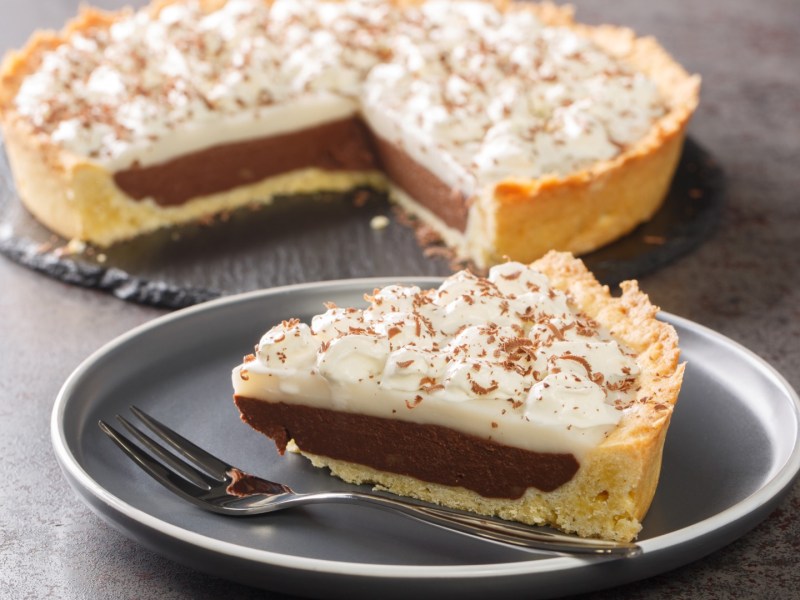A piece of haupia pie on a plate. The rest of the pie is in the background.