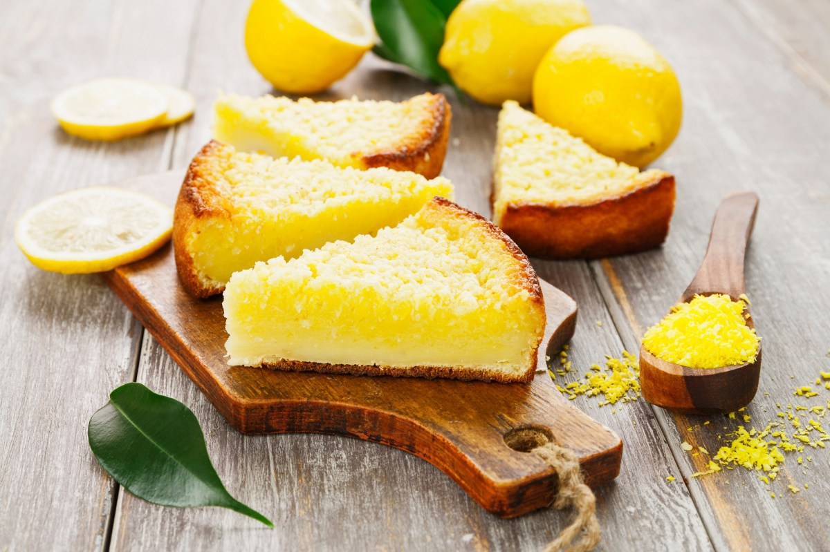 4 pieces of lemon coconut pudding cake, 3 of them on a board, surrounded by fresh lemons.