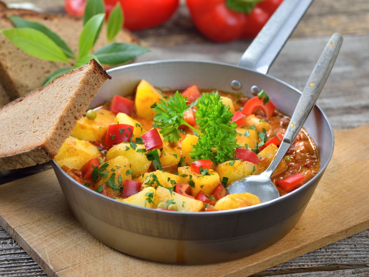 Paprika potato stew served in a pan. A spoon is in the food, a slice of bread is next to it.