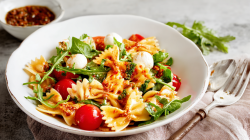 A deep plate with pasta salad, mozzarella, and red pesto.