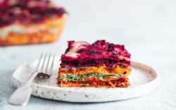 A piece of vegan rainbow lasagna on a plate. The rest can be seen in the background.