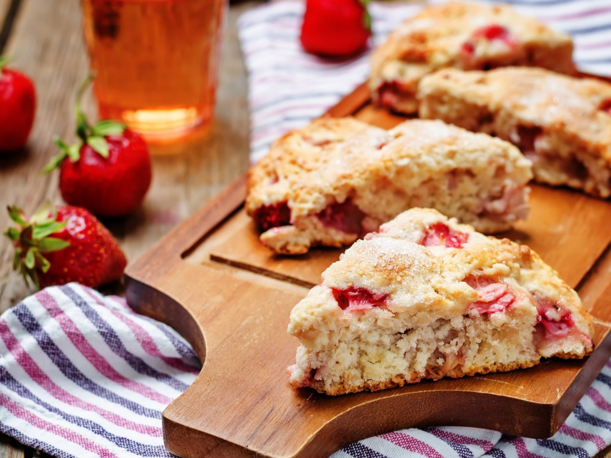 Strawberry buttermilk scones on a board, strawberries and striped kitchen towel.