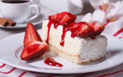 A piece of strawberry coconut cake on a plate. A cup of coffee can be seen in the background.