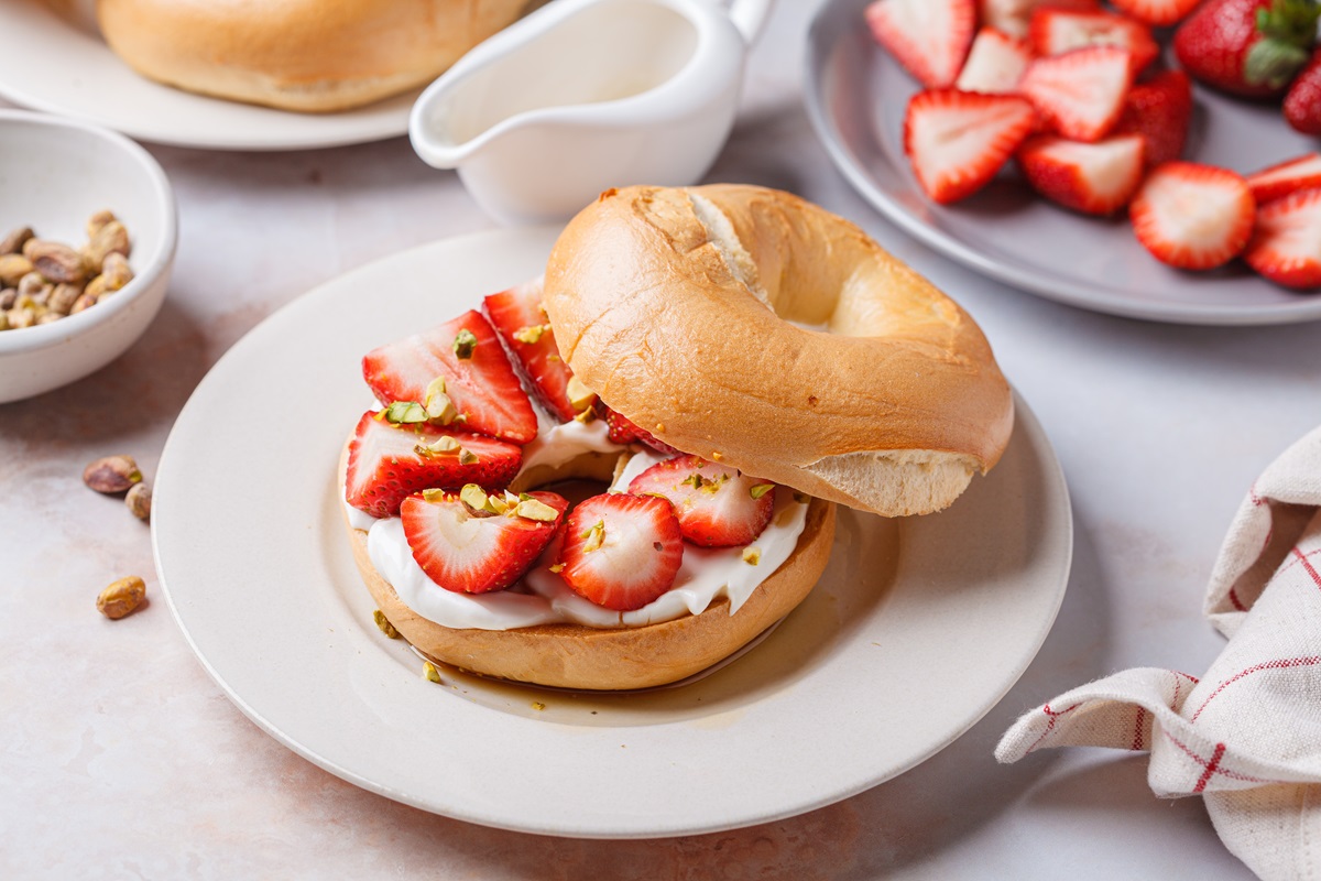 A strawberry-ricotta bagel on a white plate.
