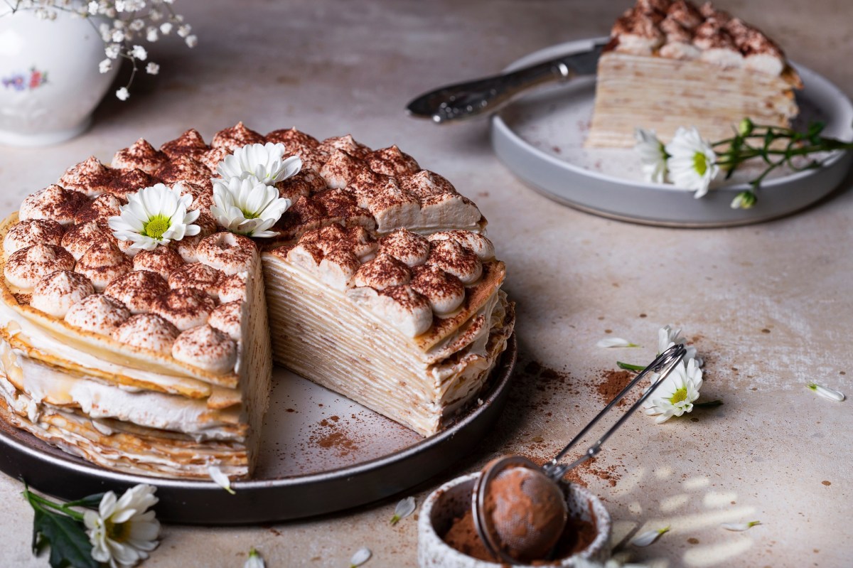 Tiramisu pancake cake, with a piece removed, on a cake plate.