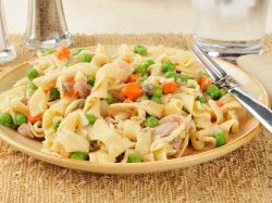 Tuna pasta with peas and carrots on a plate. Cutlery lies next to it.