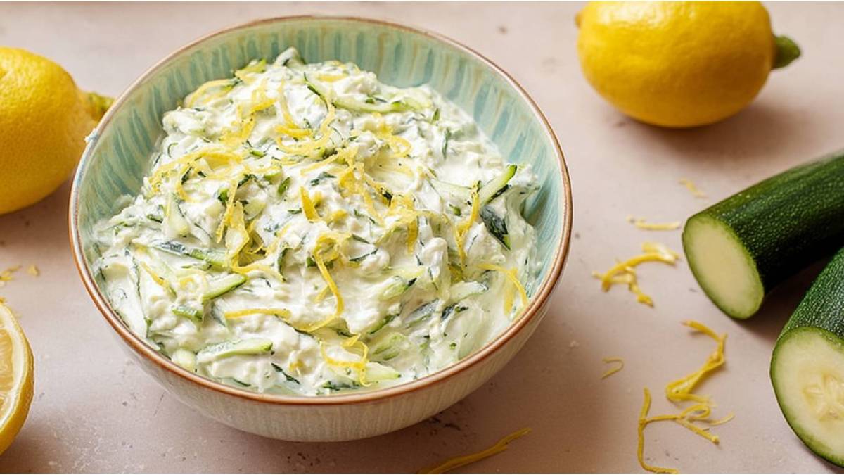 Bowl of zucchini tzatziki, zucchini and lemon next to it
