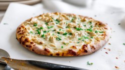 A chicken alfredo pizza with chopped parsley on top in frontal view with bright white lighting.
