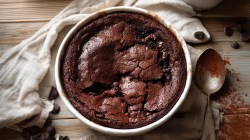A chocolate cobbler pictured from above on a table with cacao dust and chips.