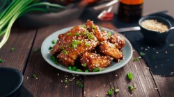 A plate of Coca-Cola glazed wings topped with sesame seeds and chopped green onions in frontal view and bright lighting.